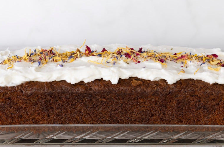 Nahaufnahme veganer Karottenkuchens mit Frischkäsefrosting und bunten Blüten 