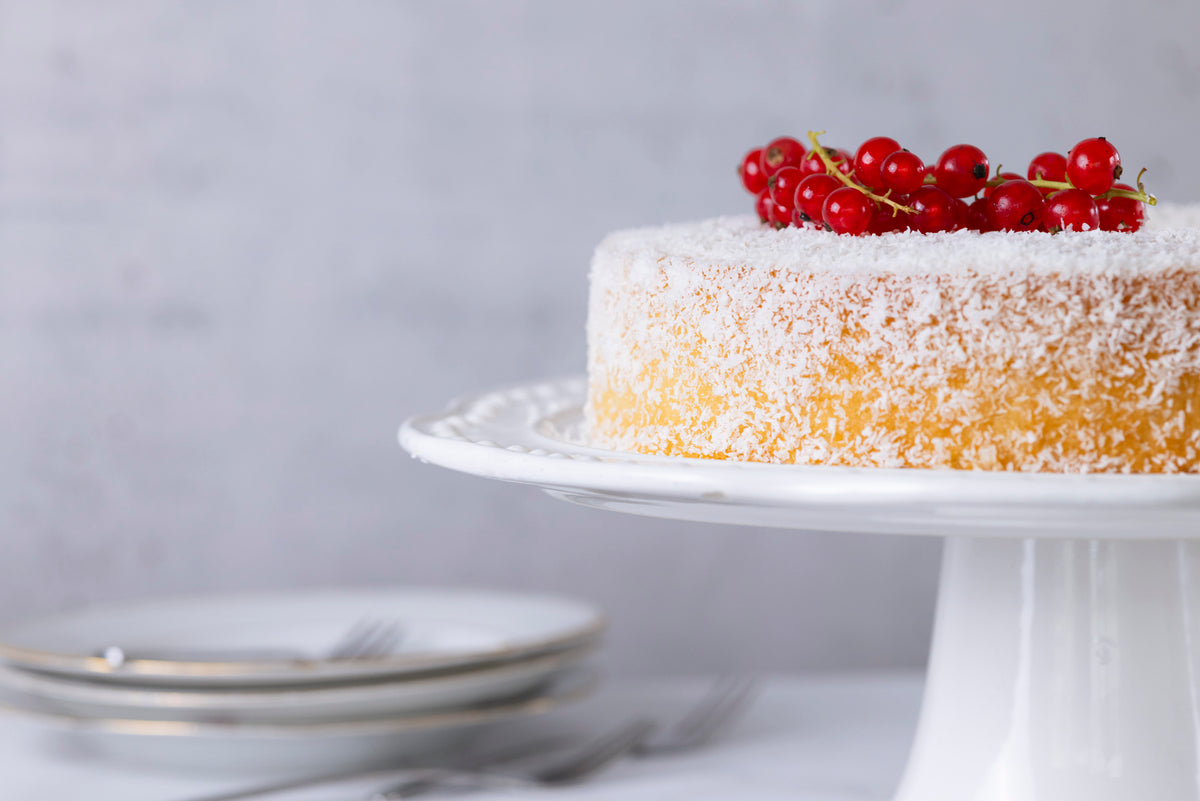 Veganer Kokoskuchen mit Kokosstreuseln und roten Johannisbeeren auf einer weißen Platte