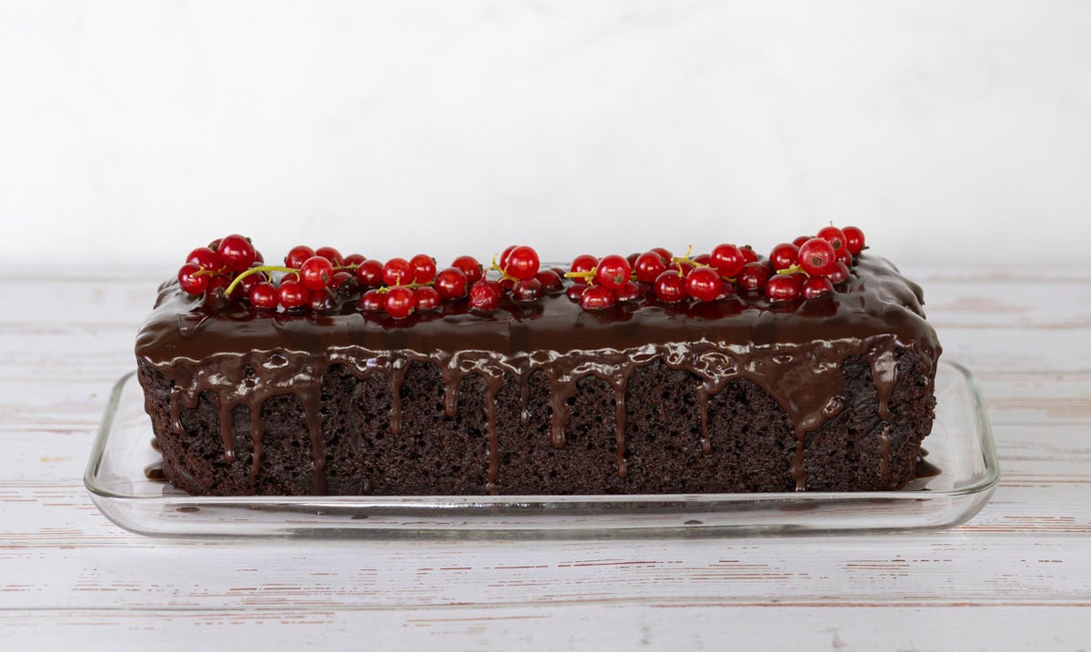 Schokokuchen in Kastenform mit einer Schokoglasur die an der Seite herunter rinnt, mit roten Johannisbeeren 